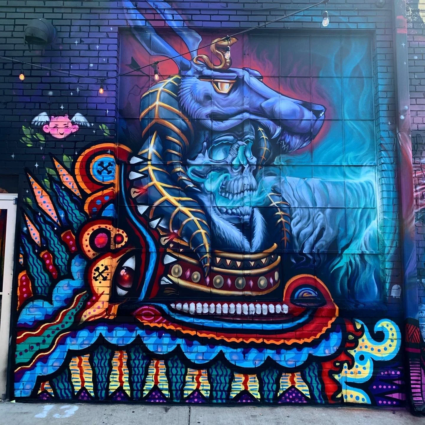 Colorful street art mural of a blue skull with a snake, dragon, and other decorative elements on a brick wall.