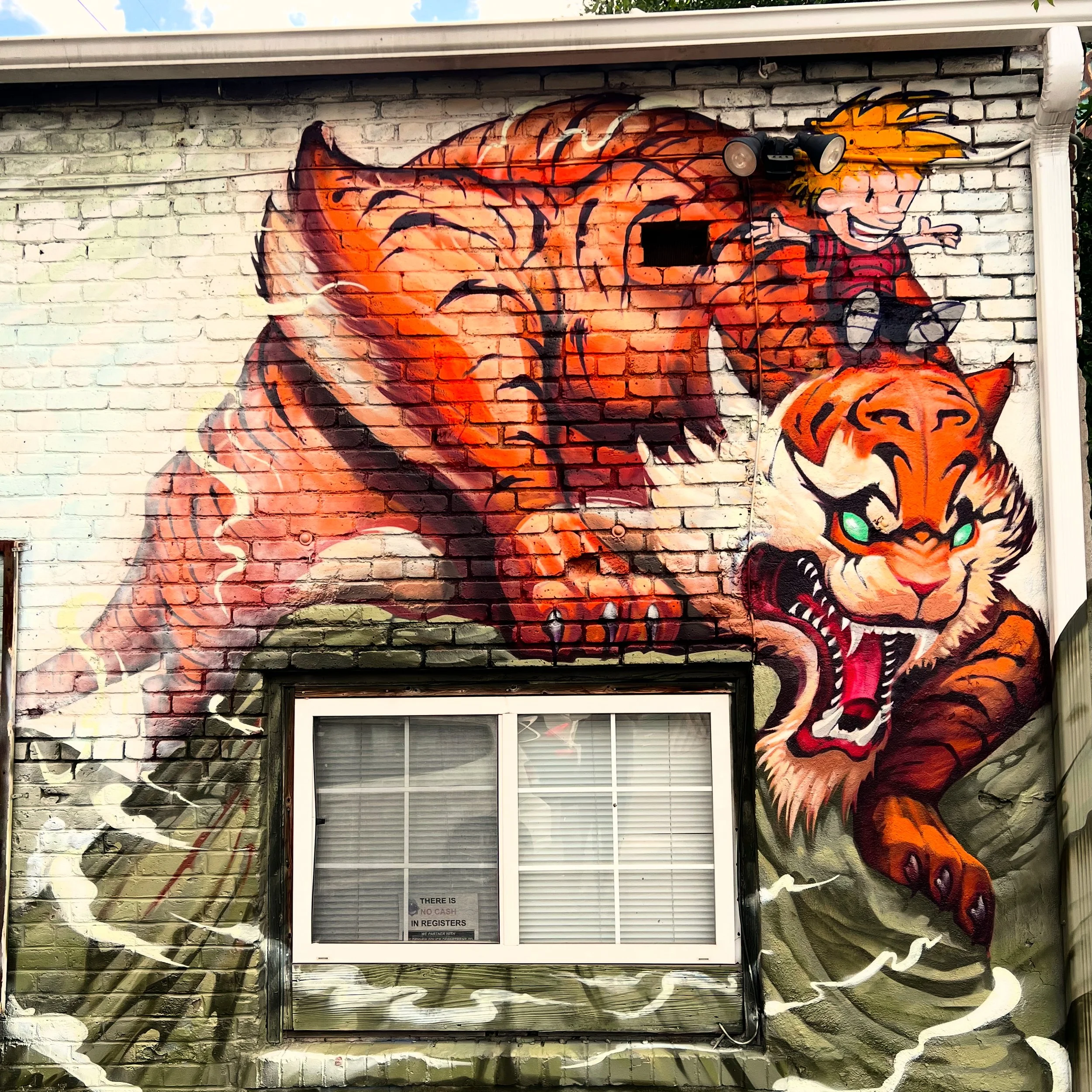 Graffiti mural on a brick wall depicting a fierce tiger and a young boy riding on its back, with dynamic lines and vibrant colors.