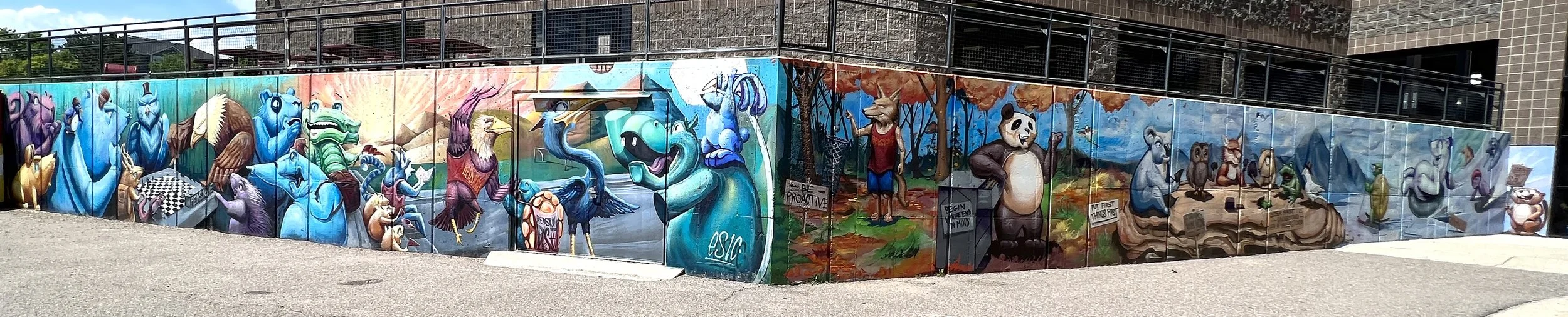 Colorful mural painting on a wall depicting various animals and characters in different scenes, including blue animals, a panda, a fox, and mice, with vibrant background elements and graffiti tags.