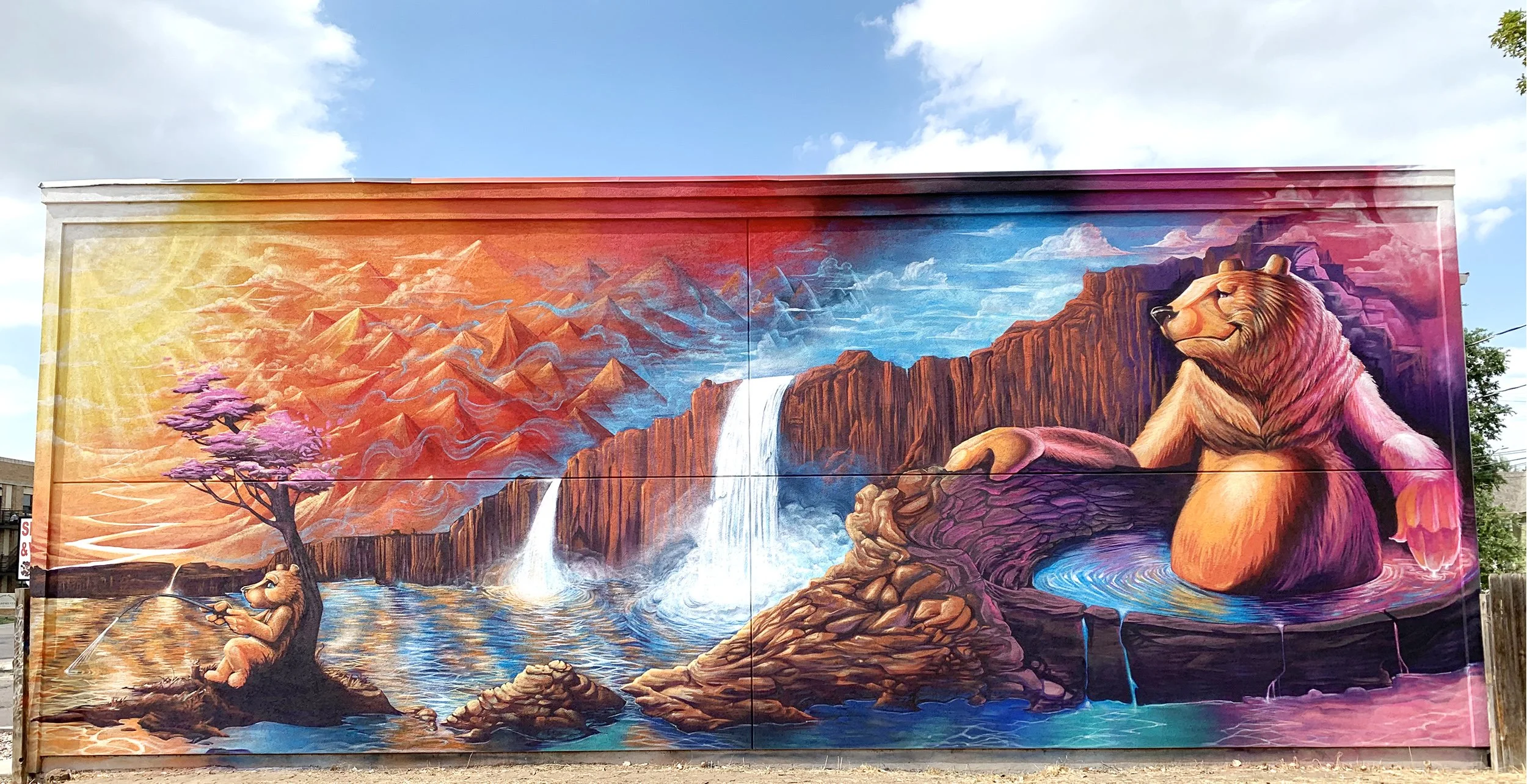 Colorful mural featuring a bear fishing by a tree near a body of water, waterfalls, mountains, and a large bear statue in a natural landscape with striking bright colors.