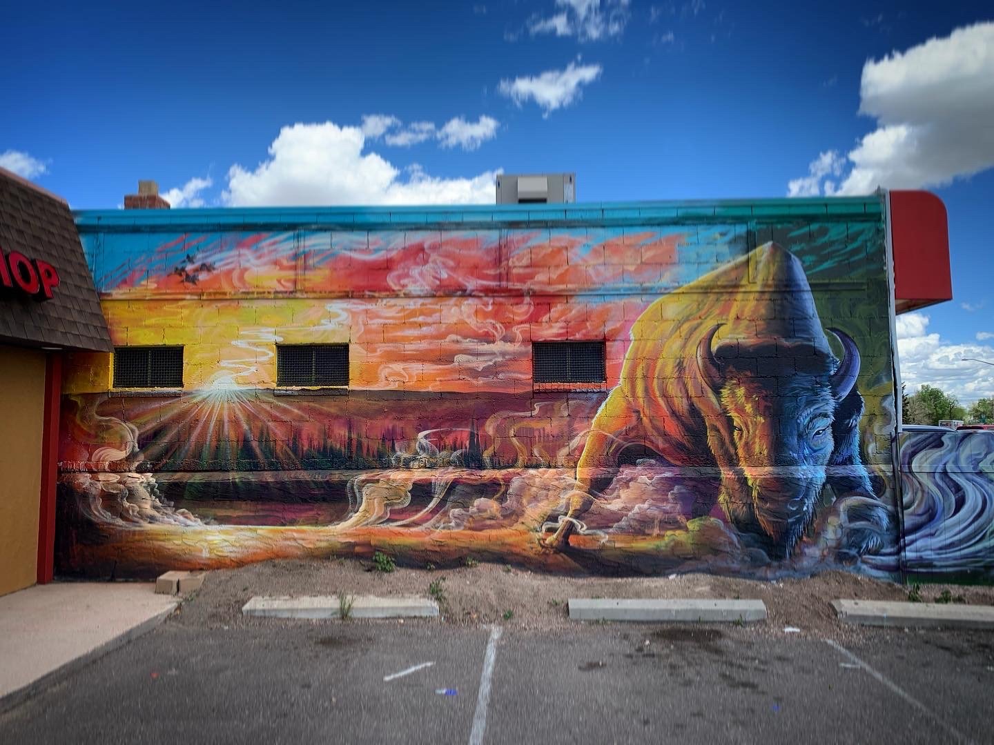 Colorful mural on a building wall depicting a bison with a mountainous landscape and a sunset in the background.
