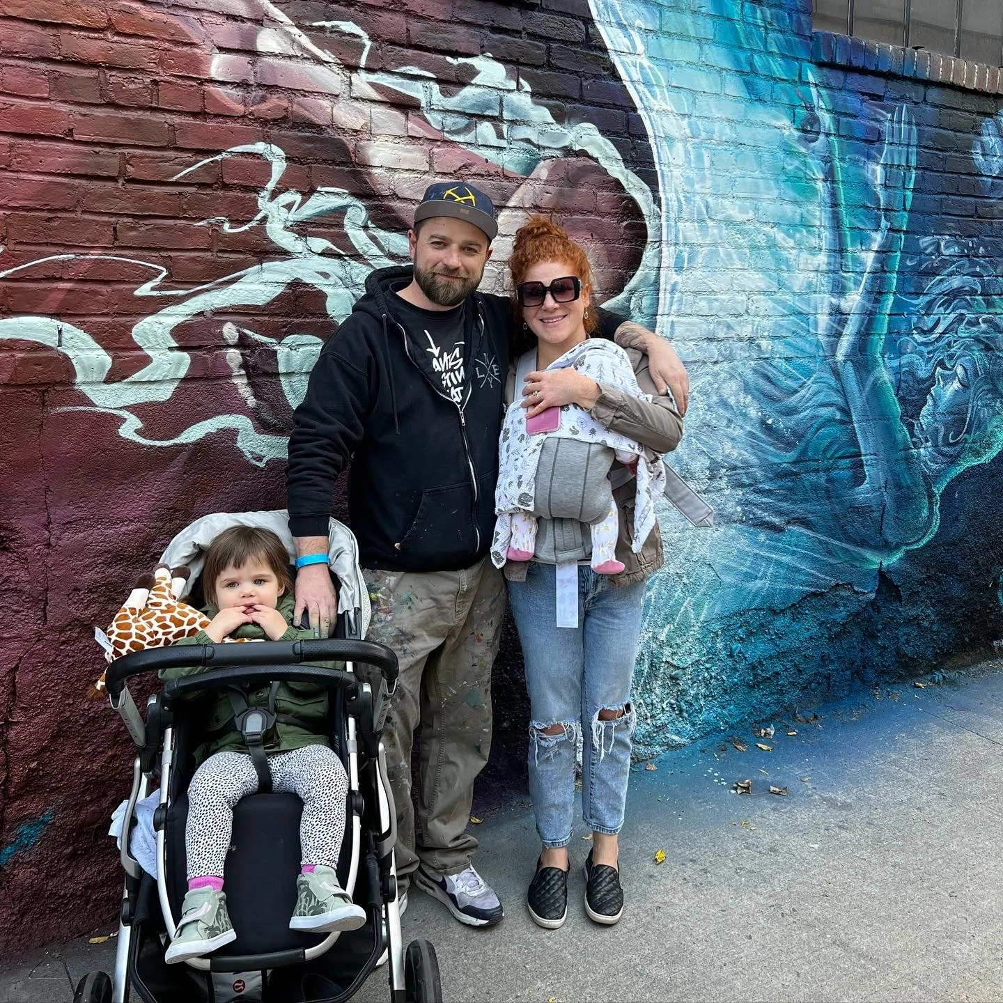 A group of four people, a man, a woman, and two children, standing in front of a large colorful mural of a whale on a brick wall.