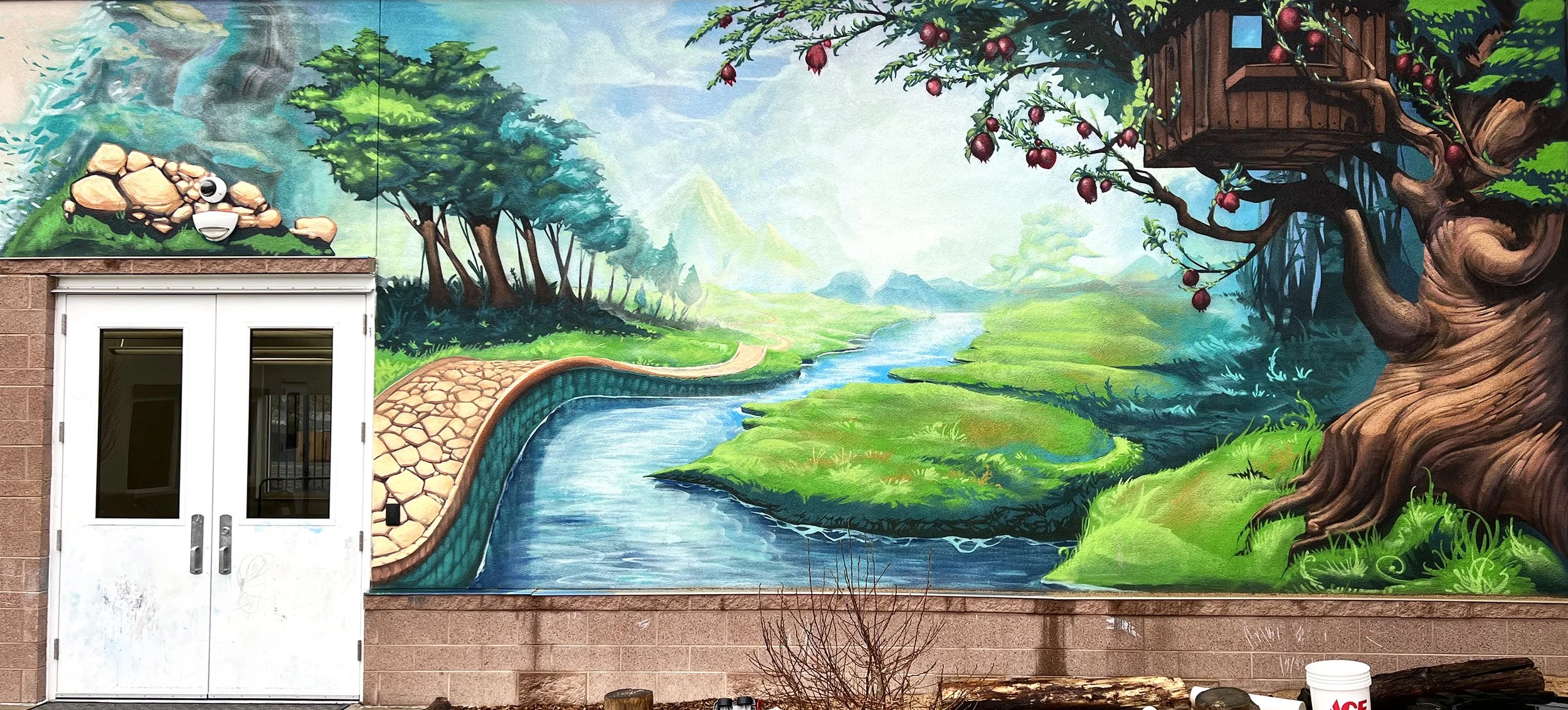 Colorful mural of a natural landscape with a river, green hills, trees, and a treehouse with red fruit on a large, stylized tree.