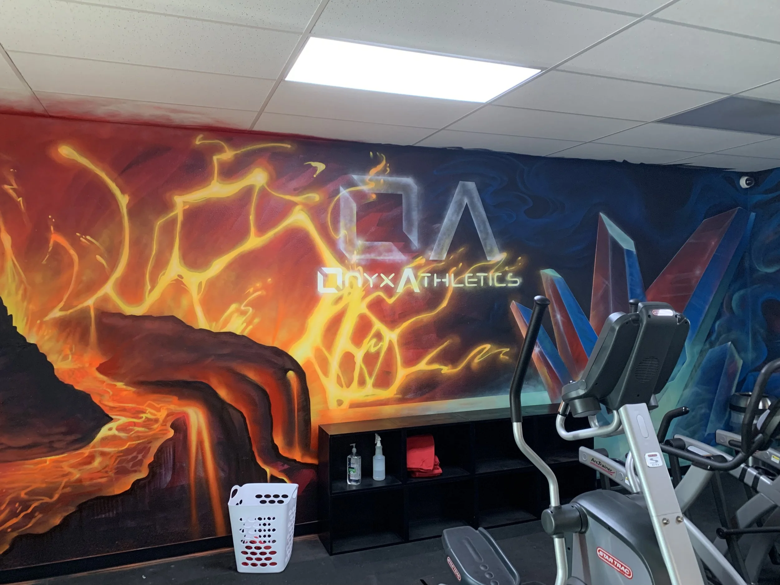 Gym with a vibrant mural of lava and flames, featuring the words 'Onyx Athletics' and fitness equipment near the wall.