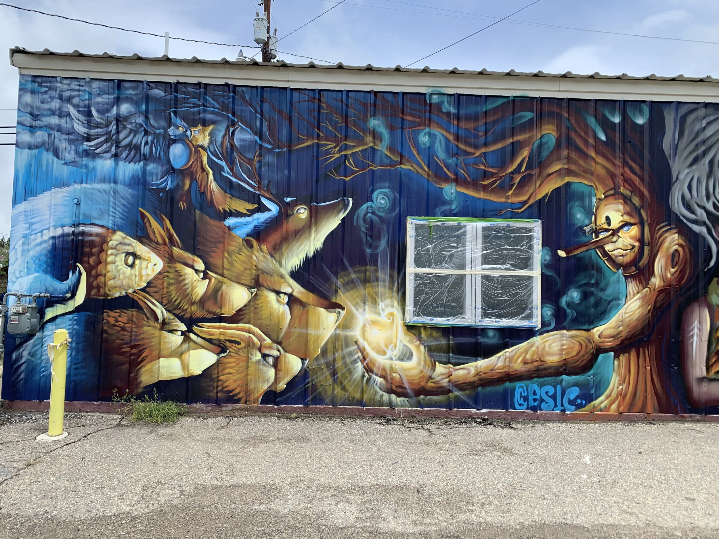 Colorful mural painting featuring a person with glasses and a pipe, extending a hand with a glowing orb towards a group of lions with a blue background, trees, and swirling blue orbs.