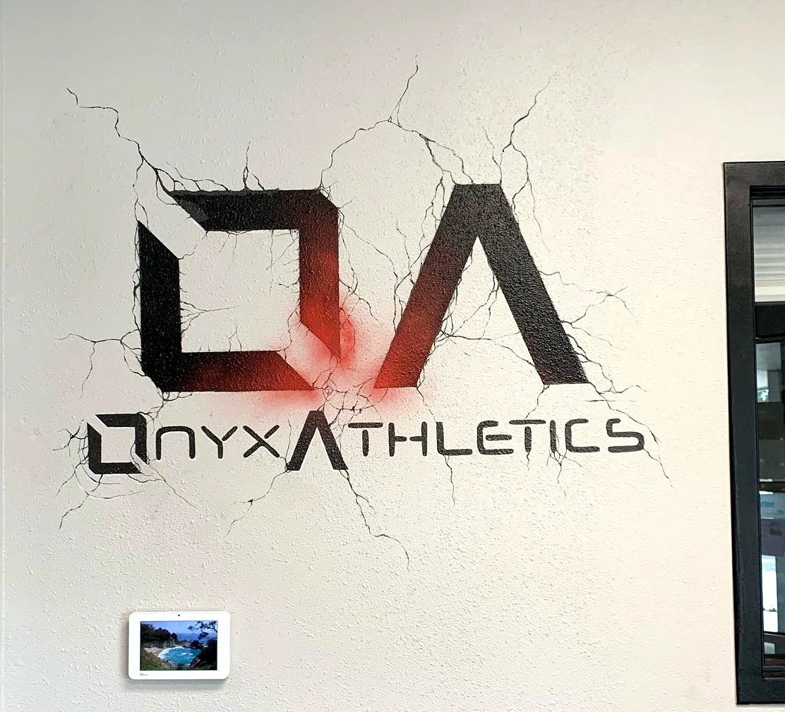 A wall with a painted logo of CQ Onyx Athletics, designed to look like it's cracked and breaking the wall, with an embedded picture of a tropical beach scene below.