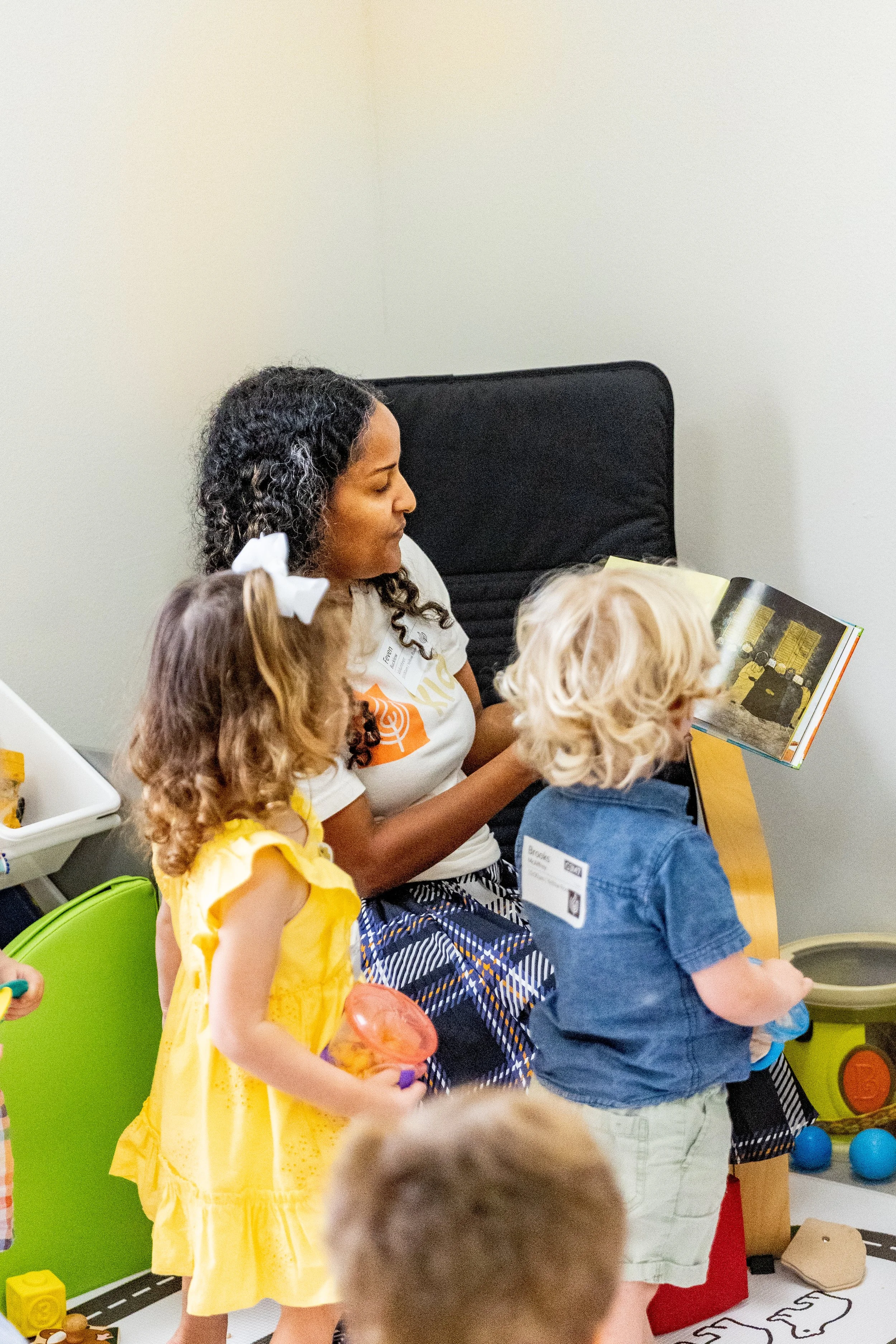 A woman reading a book to children at a play area with toys.