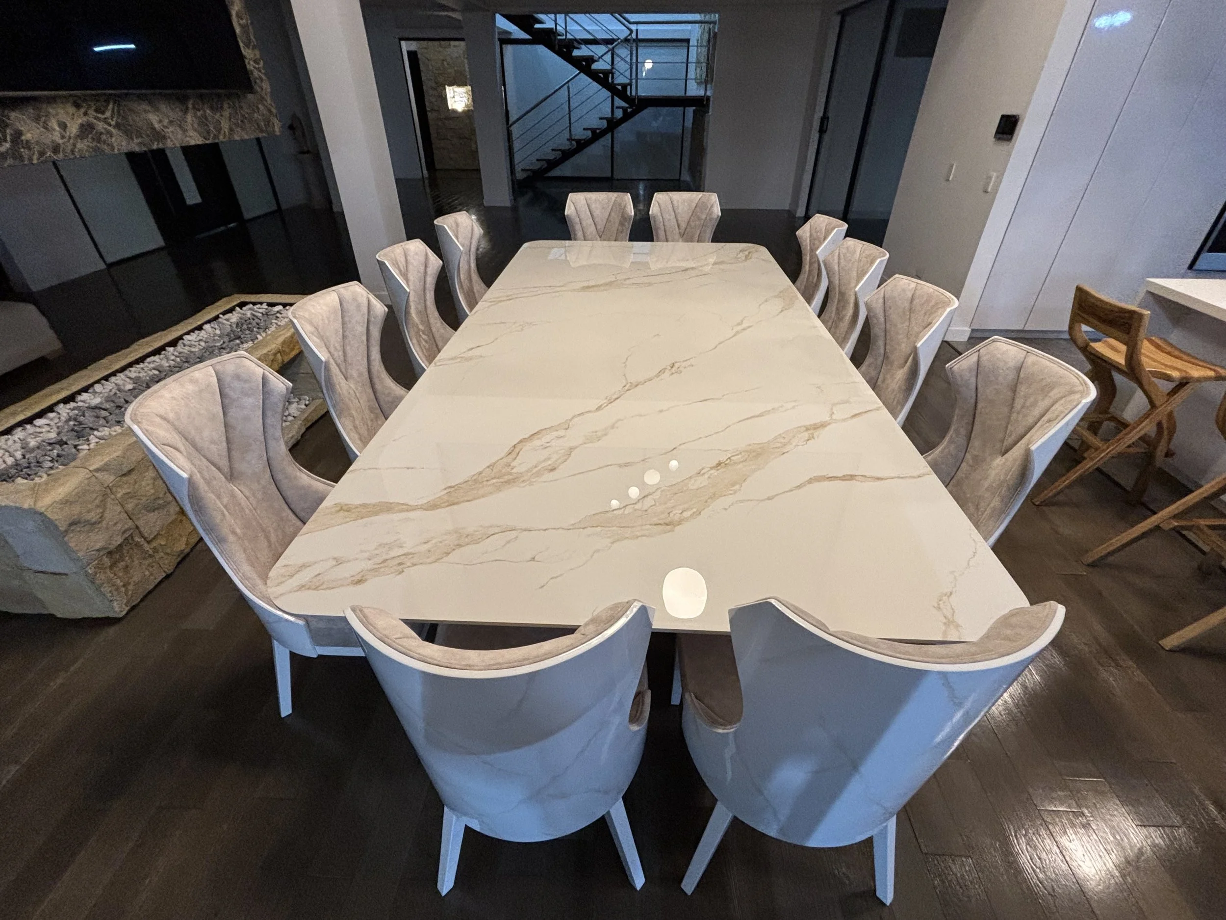 mesa de comedor de mármol con sillas elegantes en un comedor moderno con escaleras de vidrio y paredes de color neutro