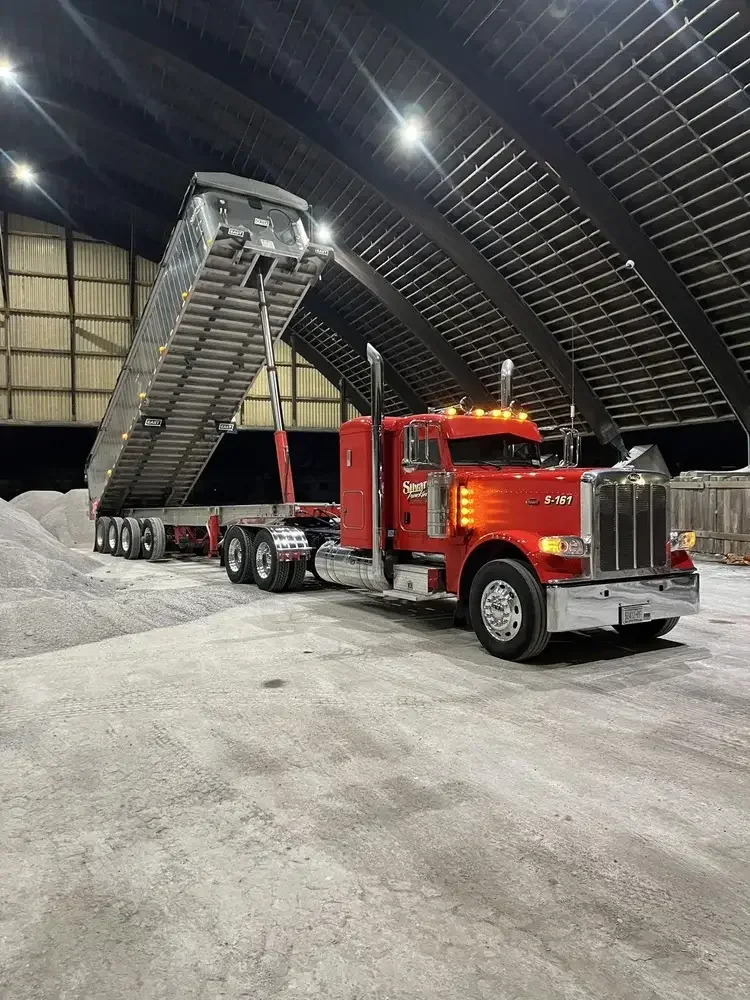 Red semi-truck in a warehouse with a raised load of gravel or sand on a trailer