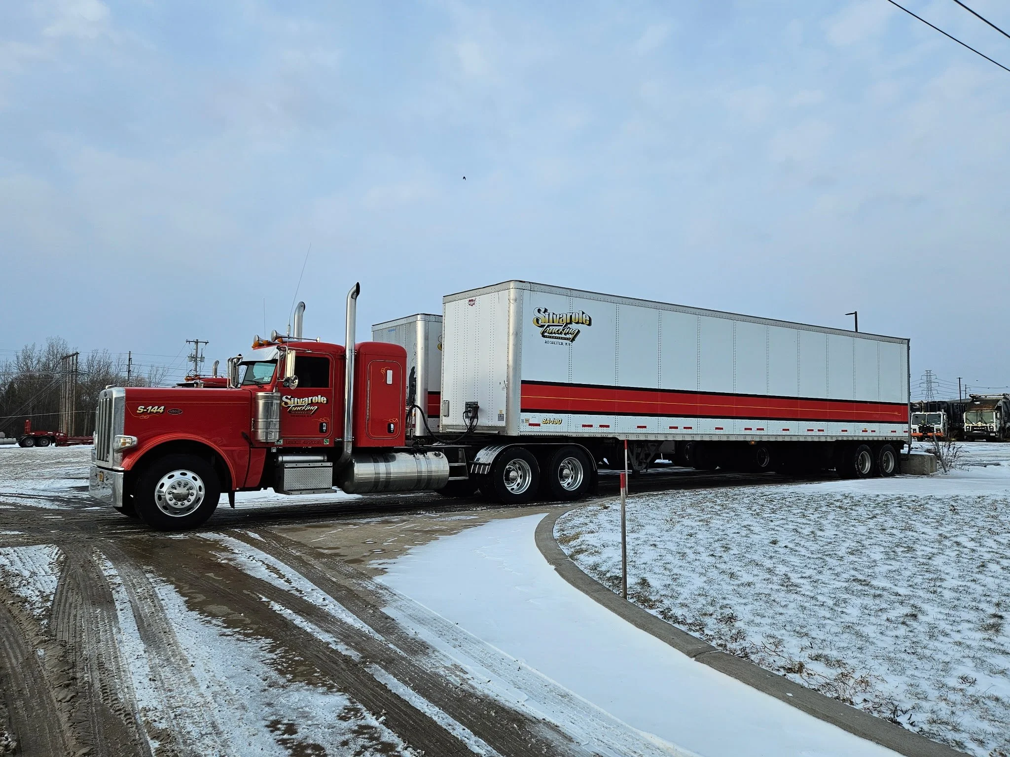 A red semi-truck with a white trailer parked on snow-covered ground.