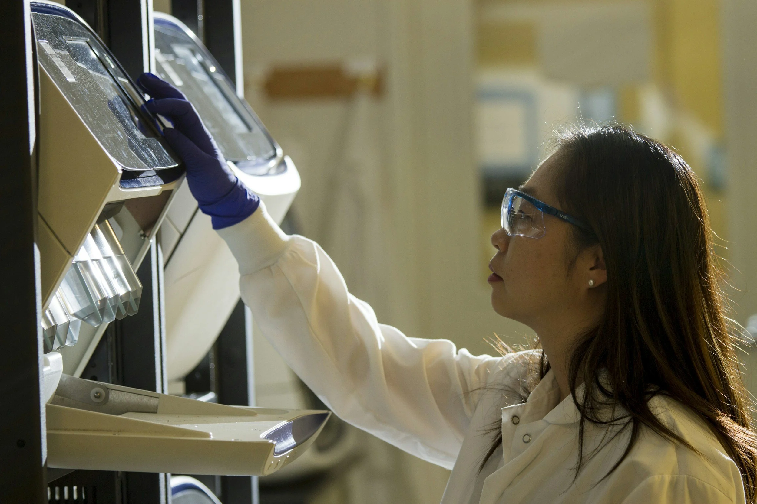 Scientist wearing safety glasses and gloves working with laboratory equipment.