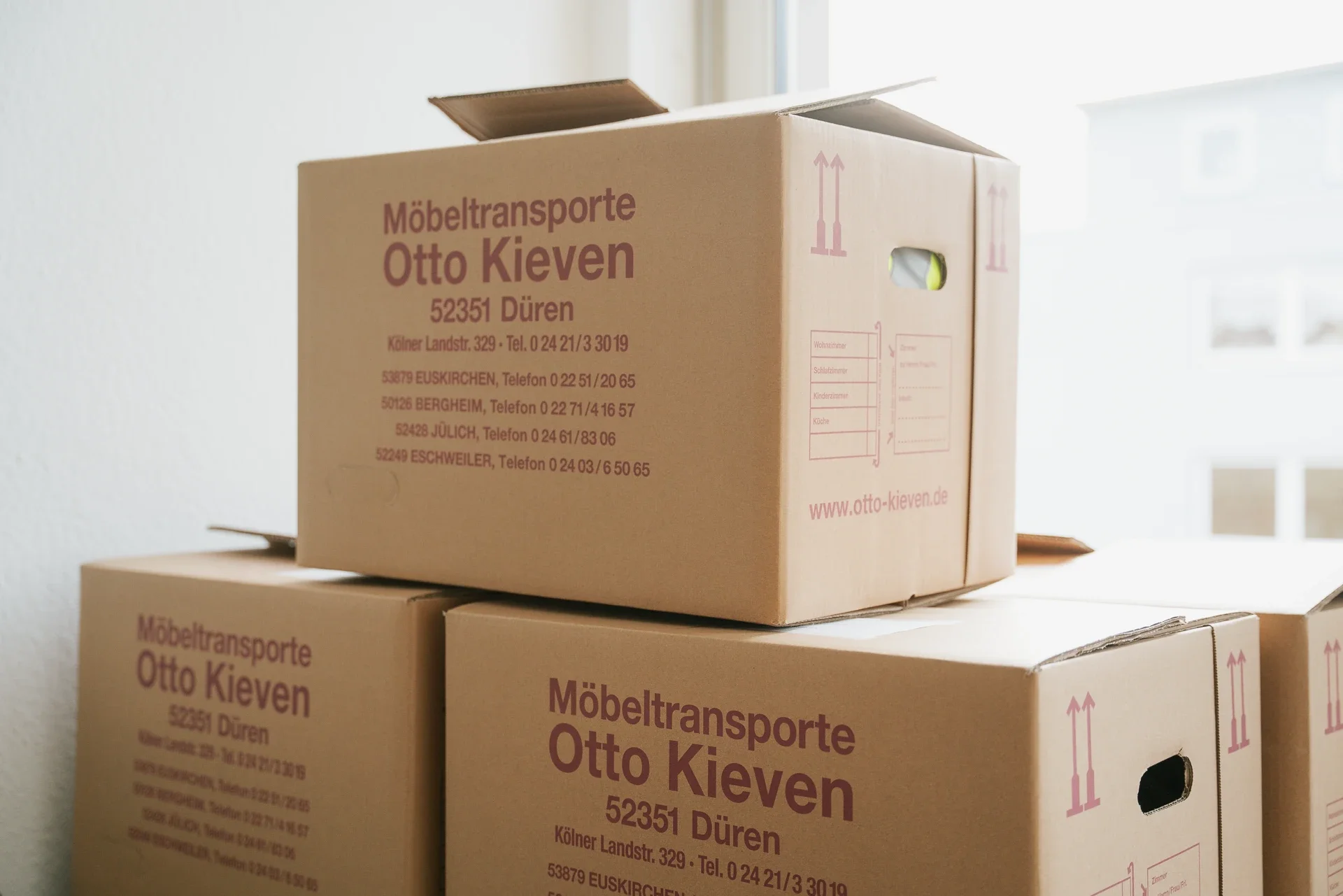 Drei Umzugskartons mit dem Logo und den Kontaktdaten einer Möbelspedition in Düren, Deutschland.