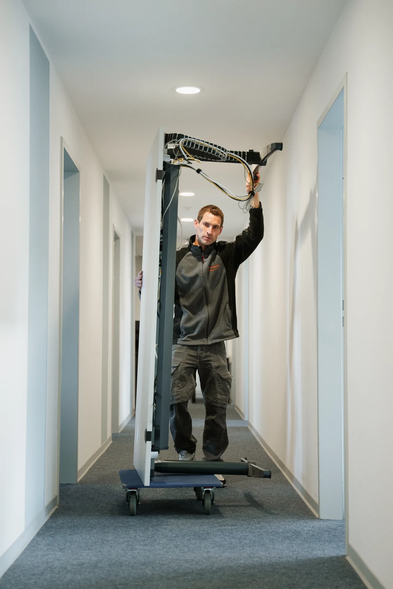 Ein Mann trägt eine große, umgedrehte Tür durch einen Flur in einem Gebäude.