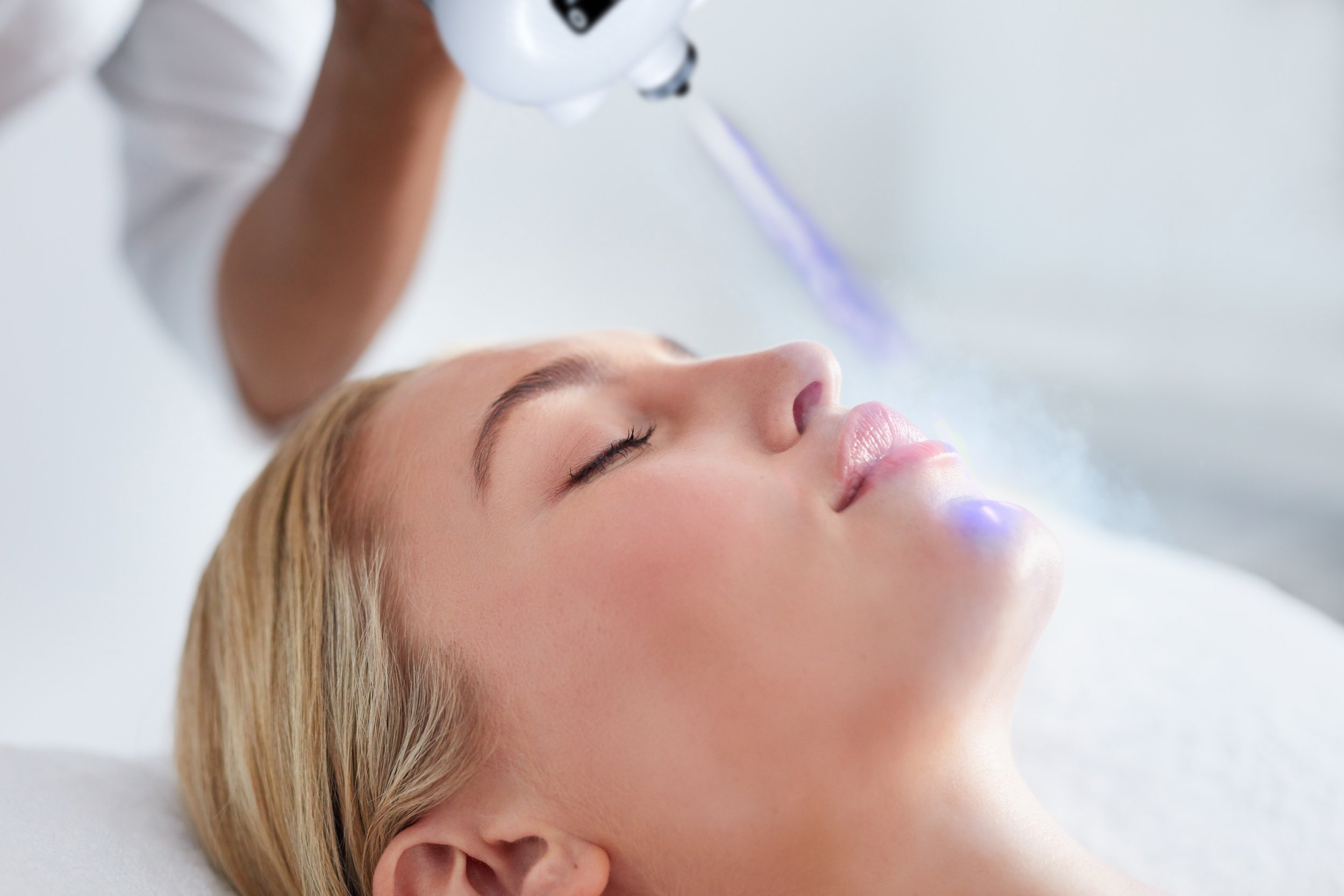 A woman receiving a facial treatment with a laser device in a spa or clinic setting.
