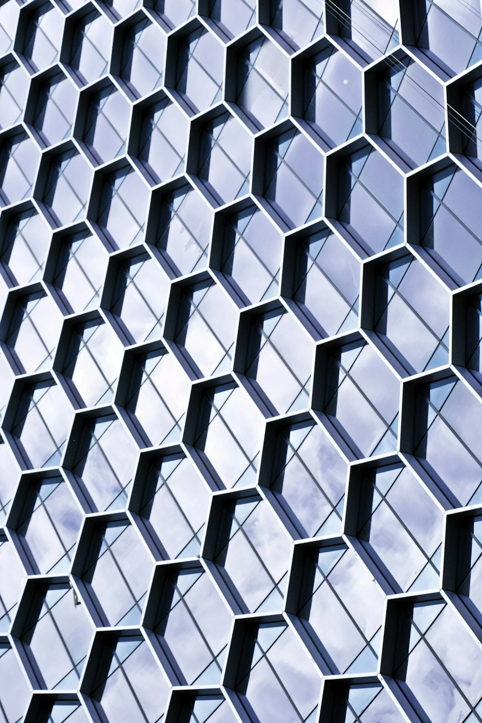 Close-up of a modern building's exterior with a honeycomb pattern of tilted glass windows and metal frames, reflecting the sky.
