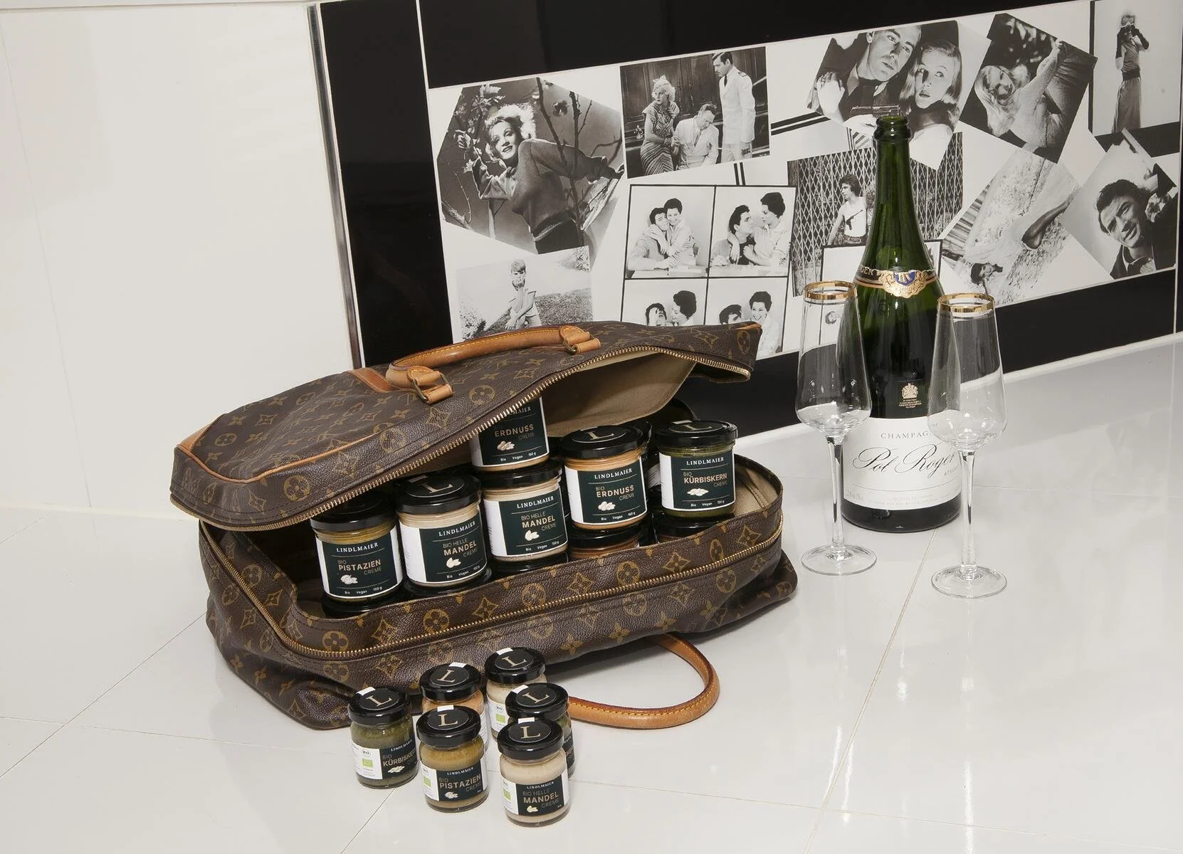 Nahaufnahme eines Leder-Koffers gefüllt mit Lindlmaier Nuss-Cremes, vor einer Badewanne mit Fliessen aus Filmszenen.