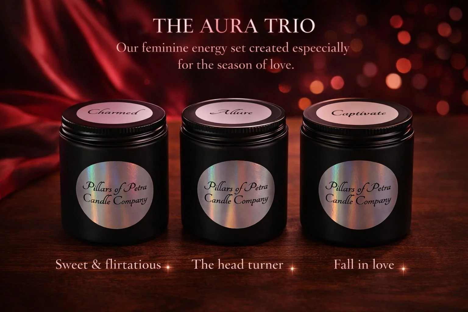 Three black candles with holographic labels from Pillars of Petra Candle Company placed on a wooden surface, each labeled 'Charmed,' 'Allure,' and 'Captivate.' The background features a red, glowing, bokeh effect with red fabric draped on the left side. Text above the candles reads 'The Aura Trio' and describes them as a feminine energy set created especially for the season of love. Text below the candles reads 'Sweet & flirtatious,' 'The head turner,' and 'Fall in love' with small star-like icons.