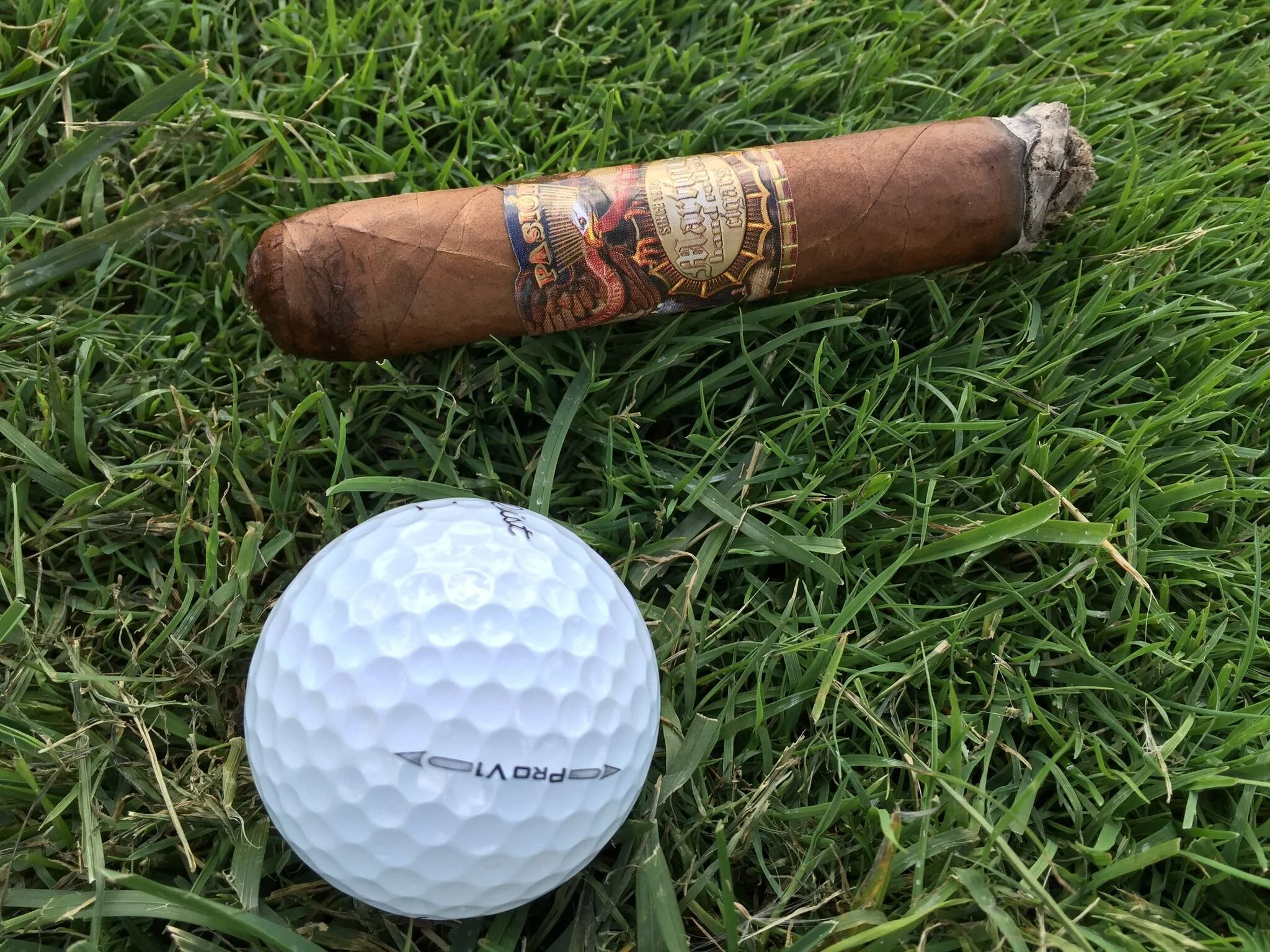 A cigar and a golf ball on the grass.
