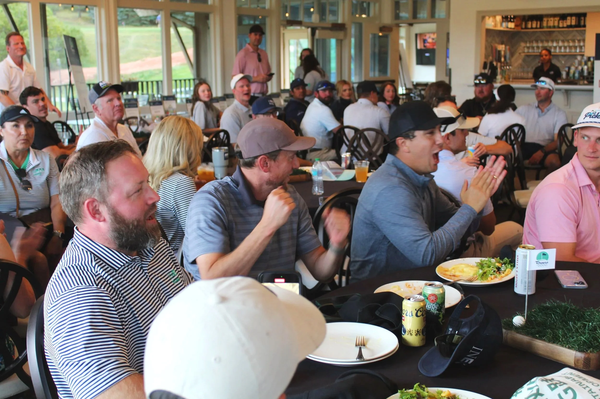 Group of people seated at tables enjoying a meal at a social event, with some chatting and others watching or listening.