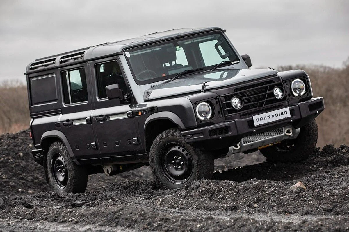 Black Land Rover Defenders off-road vehicle on dirt terrain with a cloudy sky