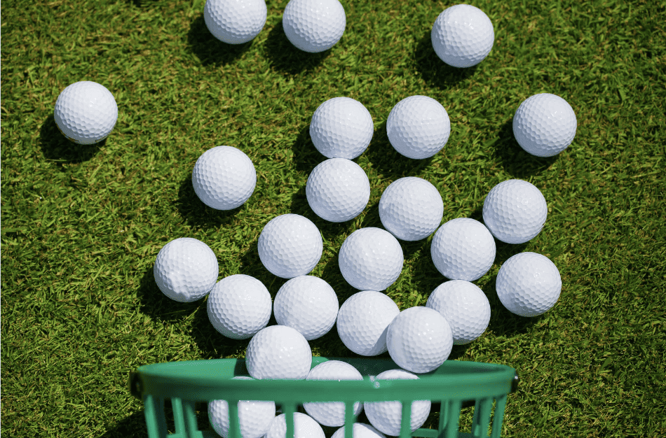 Golf balls on green grass with some inside a green basket.