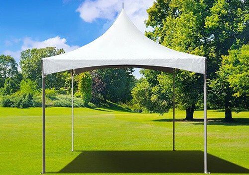 A white outdoor event tent set up on a grassy field with trees in the background and clear blue sky.