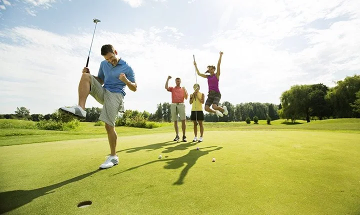 Four people celebrating on a golf course with a man kicking his golf club in the air and three others cheering.