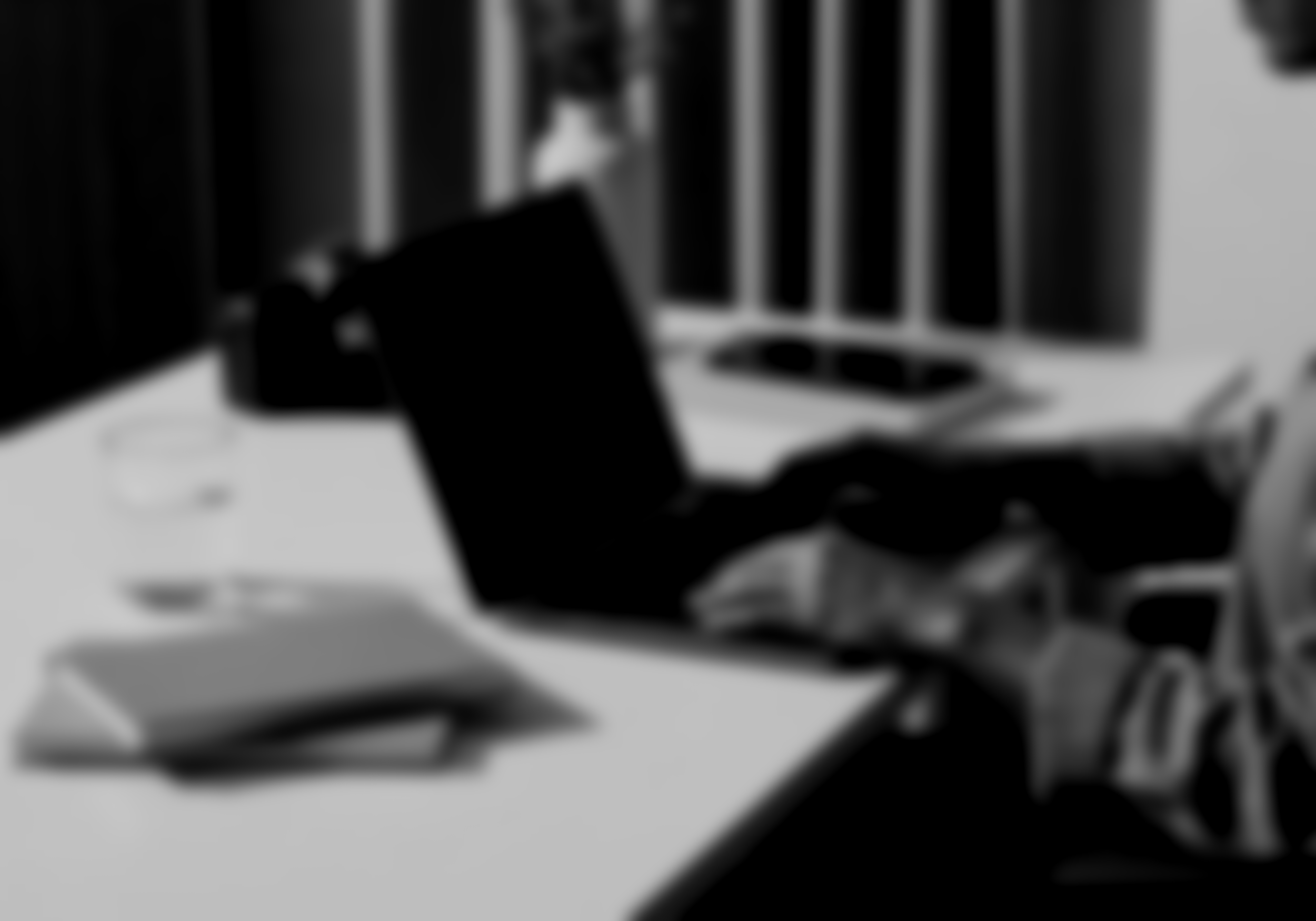 Blurred image of a desk with a closed laptop, a notebook, and a glass of water.