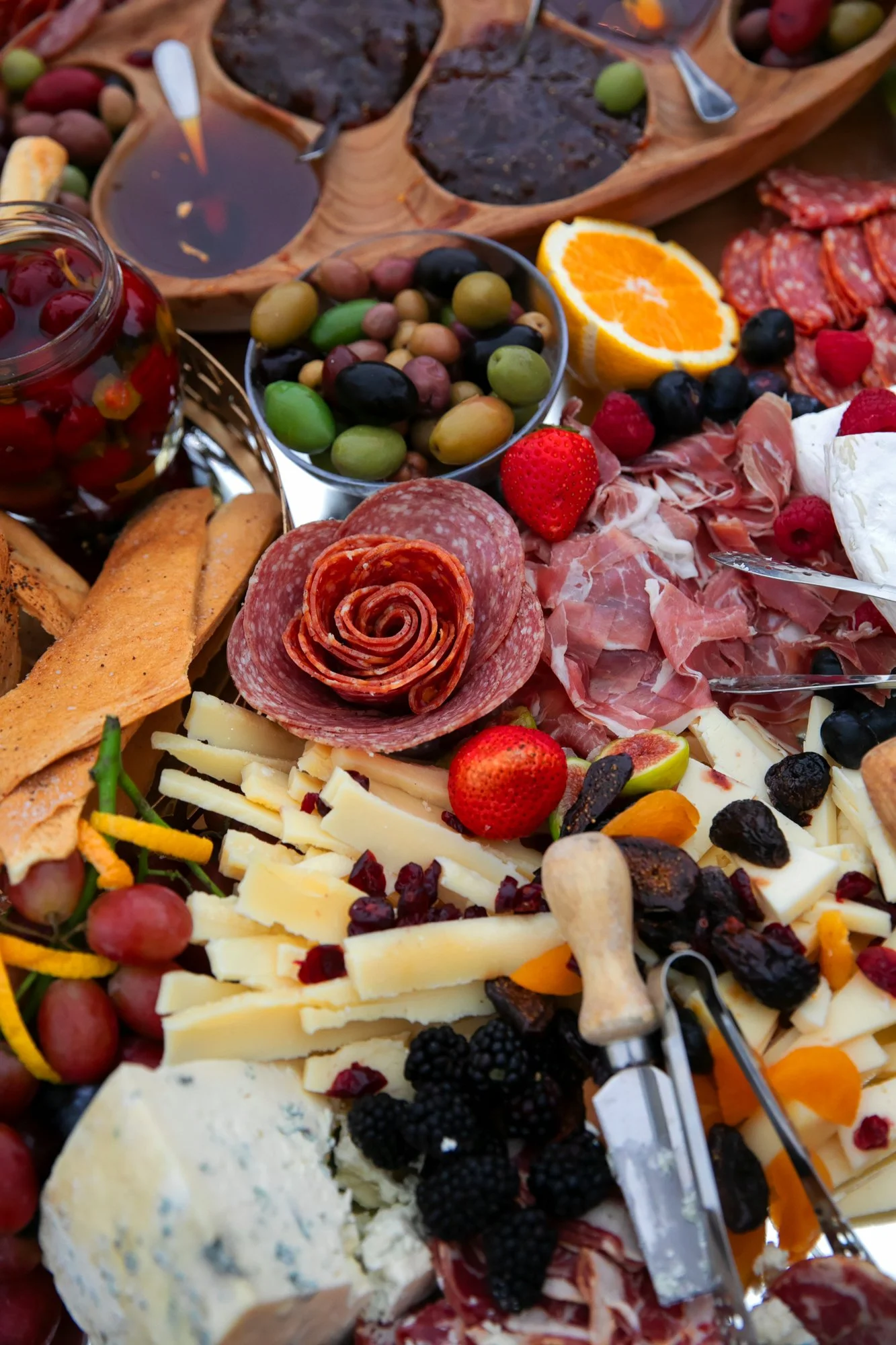 A spread of assorted cheeses, cured meats, fresh fruits, jams, and crackers, typical of an outdoor charcuterie platter.