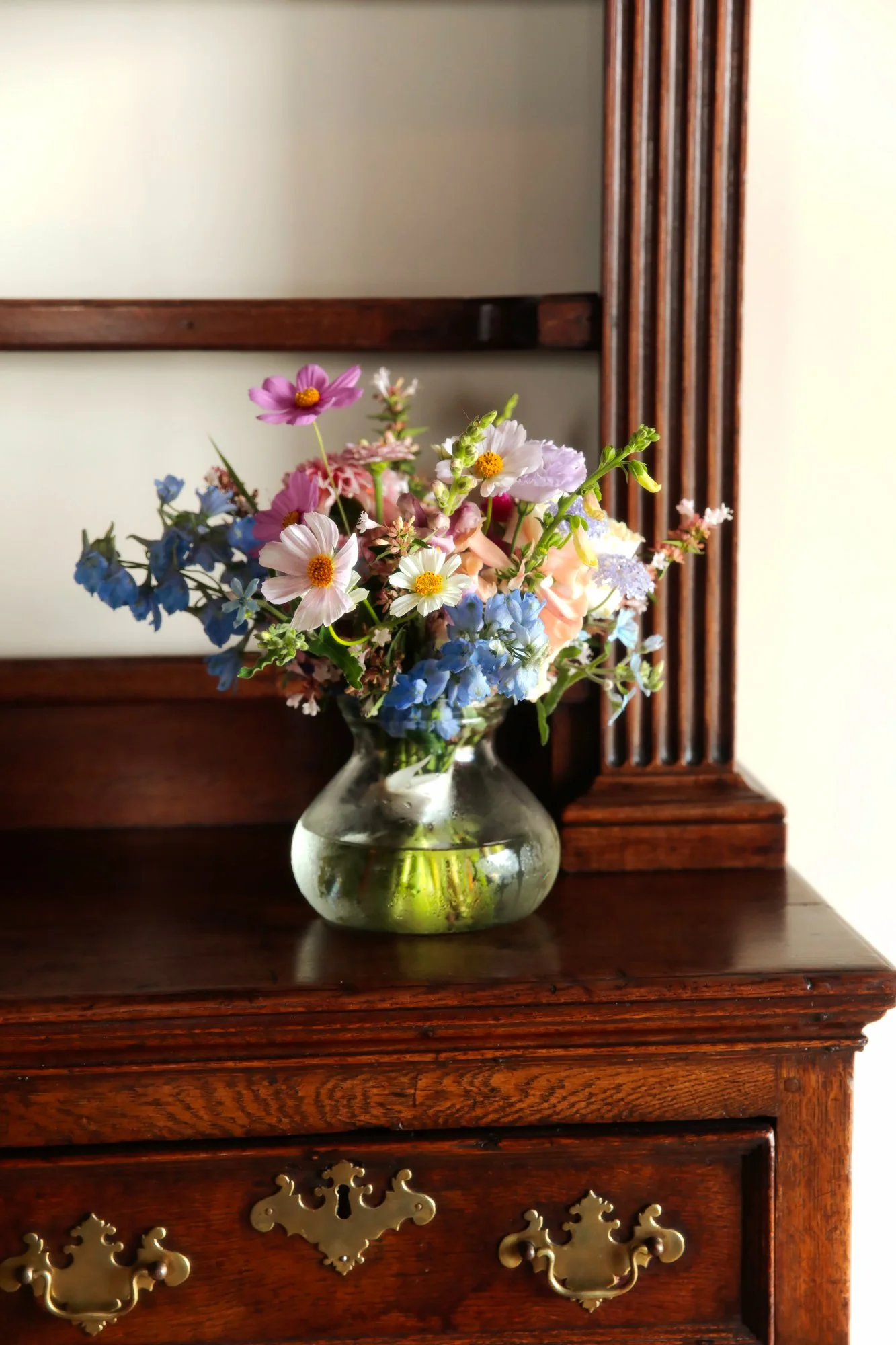 A bouquet of colorful flowers in a glass vase on a wooden dresser with a mirror behind.