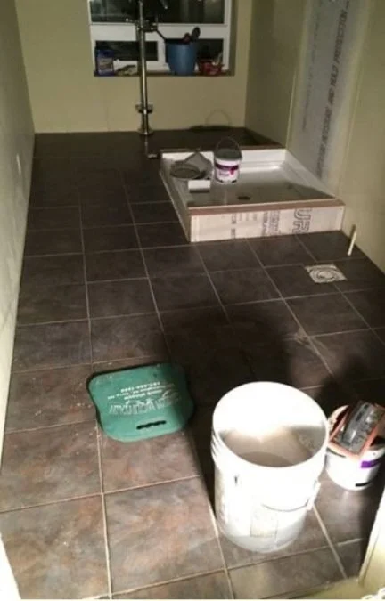 A bathroom under construction with a partially installed shower, a bucket, and construction tools on the floor.