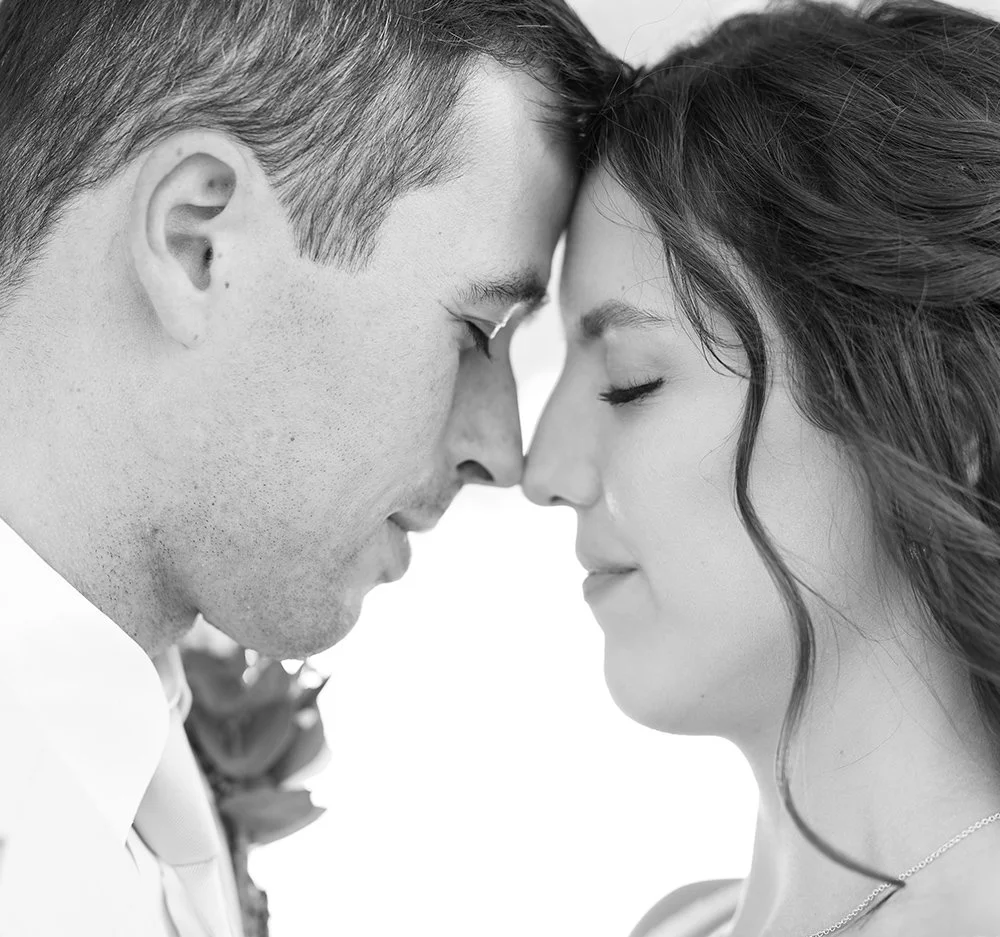 A black and white close-up of a couple with foreheads touching, eyes closed, sharing an intimate moment. romantic wedding photo