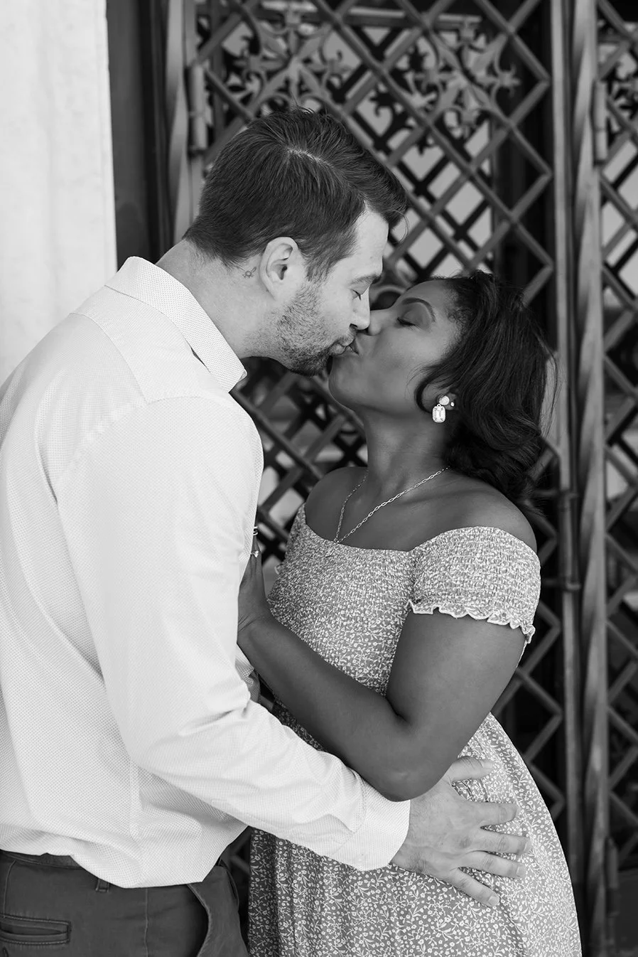 A black and white photo of a man and woman kissing, with the man holding the woman around her waist and the woman’s hand on the man’s back. Engagement photo at DIA in detroit
