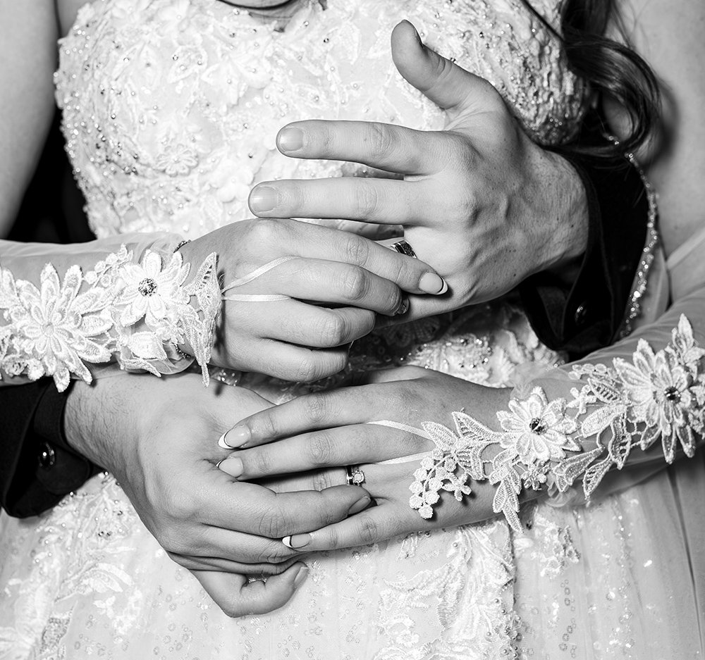 Close-up of a couple's hands on their wedding day, with the bride wearing romantic lace sleeves and both wearing wedding rings.