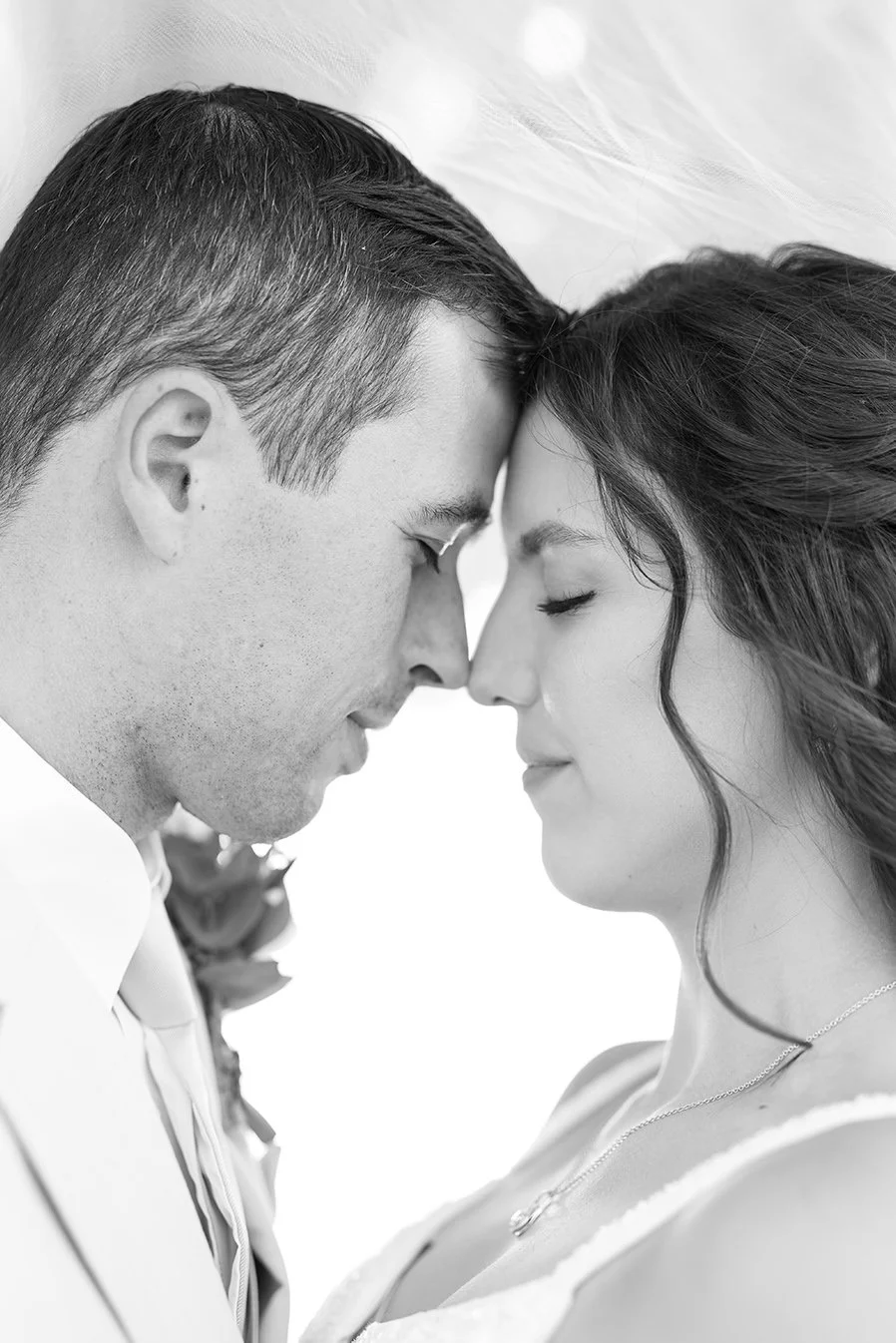 A black-and-white photograph of a couple with foreheads touching and eyes closed, sharing an intimate moment during their romantic photo session.