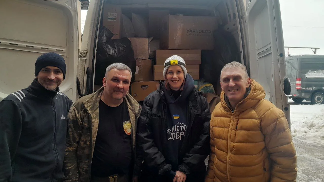 Four people standing in front of an open delivery truck filled with boxes and bags, on a snowy day.