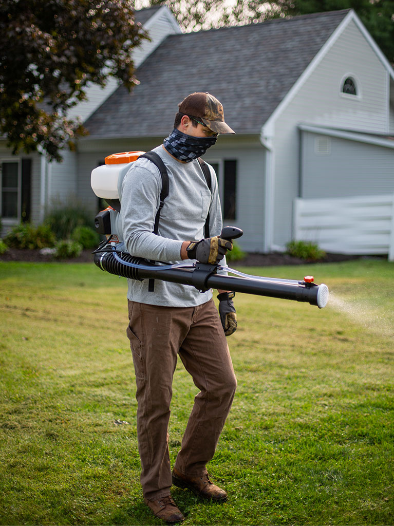 Pest control technician applying mosquito treatment in an Alaska residential yard in the Mat-Su Valley