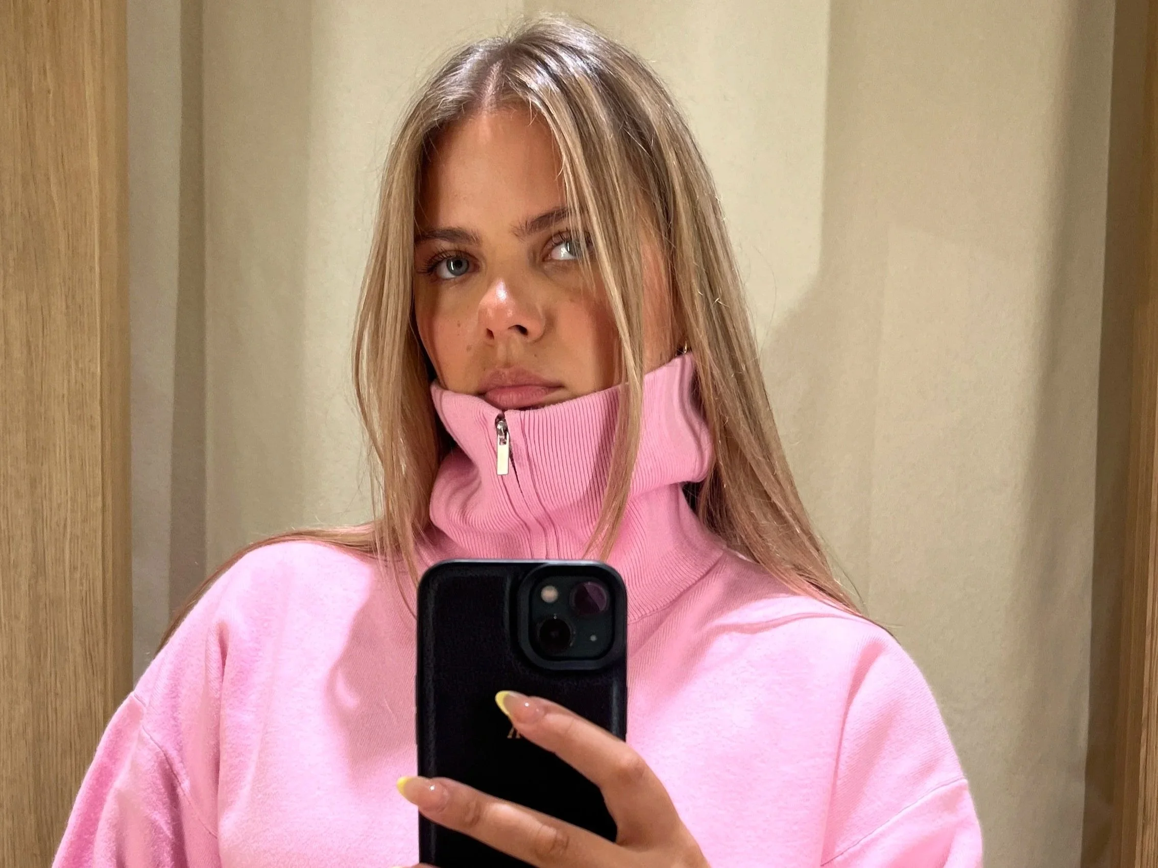 Junge Frau in rosa Pullover macht Selfie vor Spiegel im Raum.