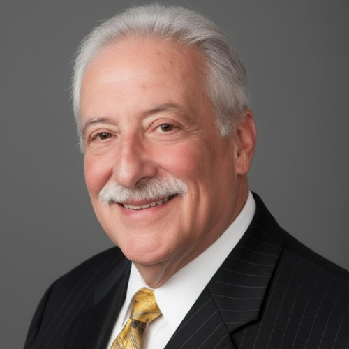 Portrait of an older man with white hair and a gray mustache, wearing a black pinstripe suit, white shirt, and a gold tie, smiling against a gray background.