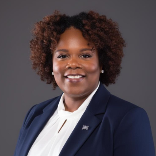A professional woman with dark curly hair wearing a navy blazer and white blouse, smiling against a gray background.