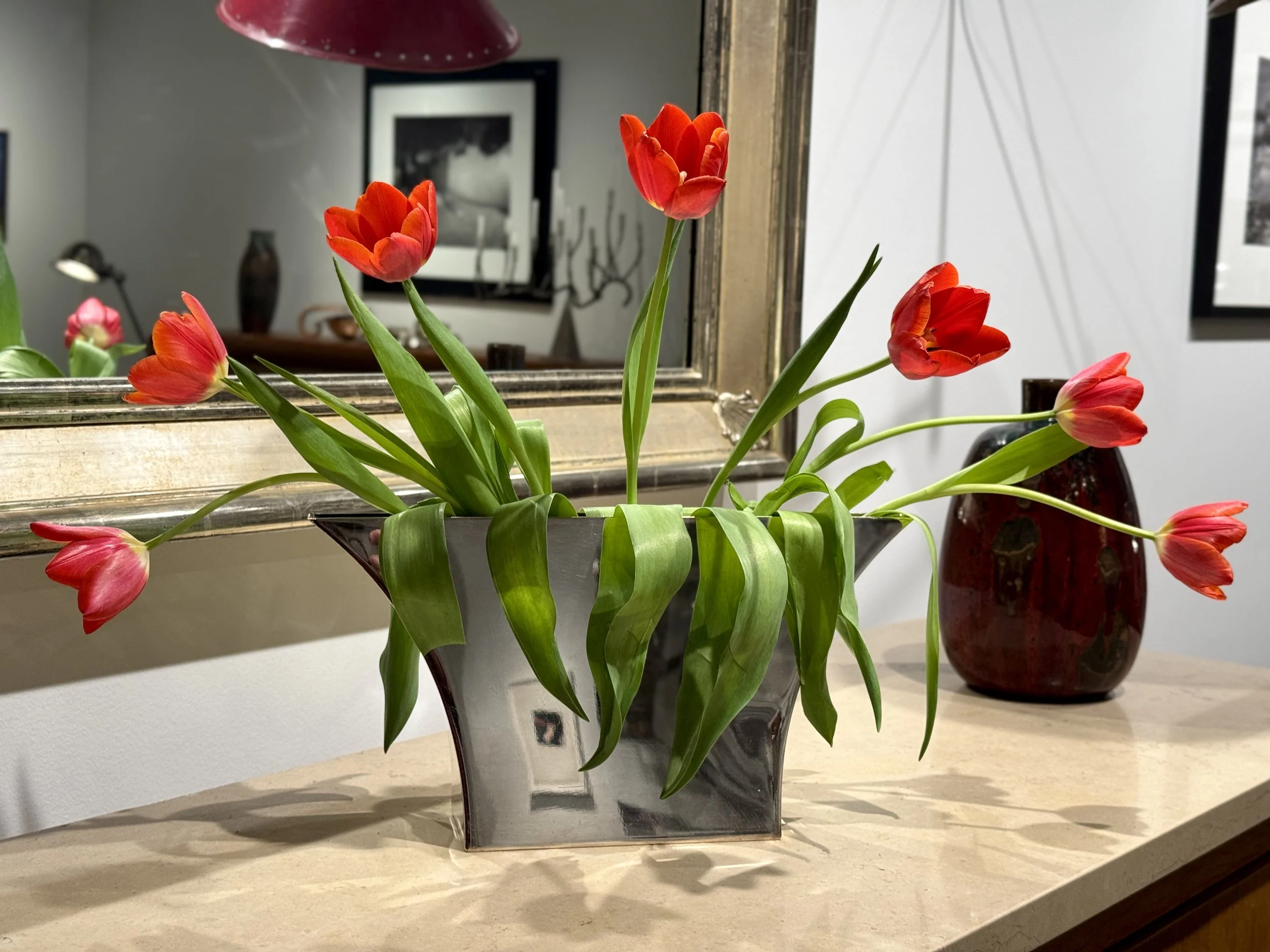 Red tulips in a gray and black striped vase in front of a mirror on a beige countertop.