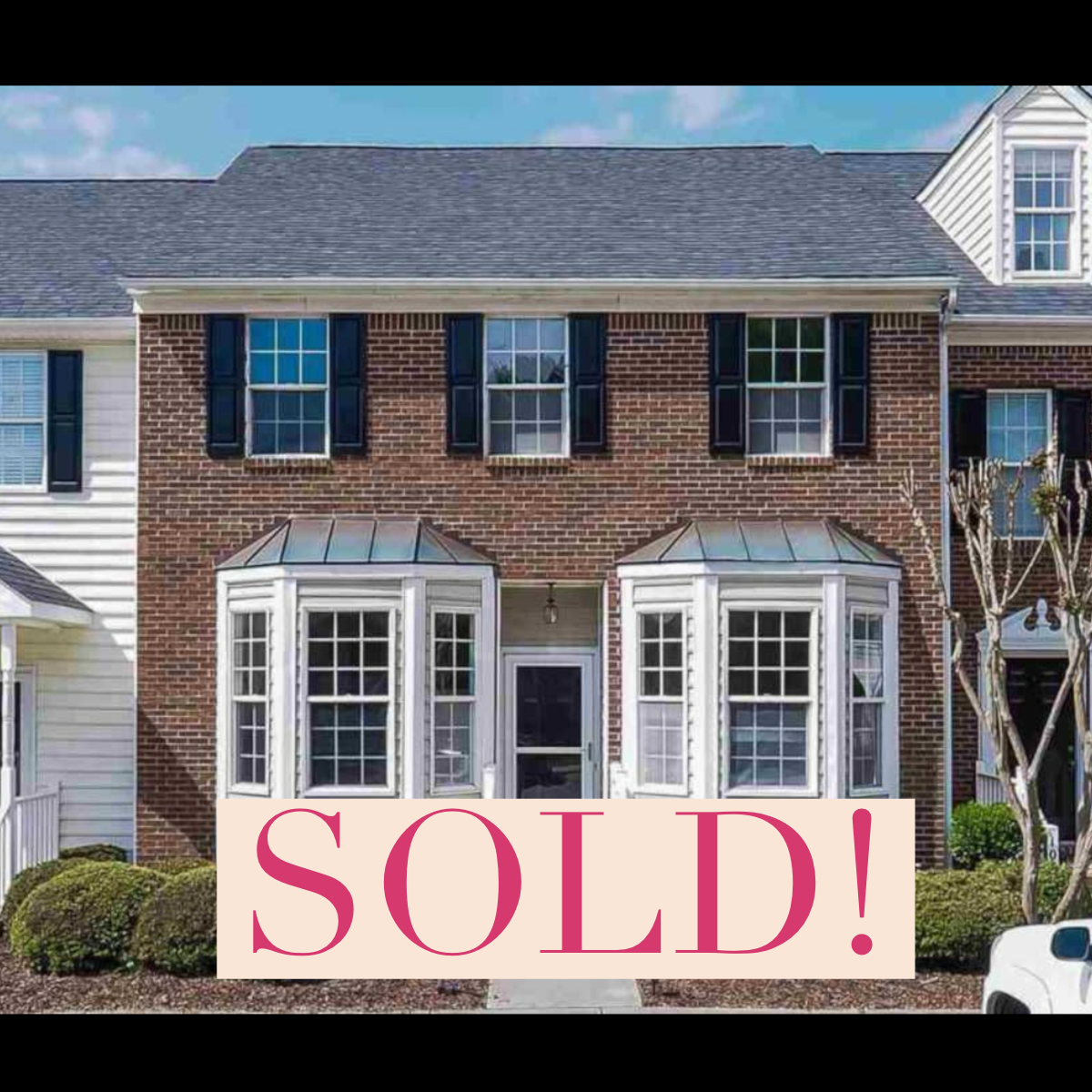 A three-story brick house with white window framing and black shutters, featuring a bay window on the ground floor, and a sign that says 'SOLD!'