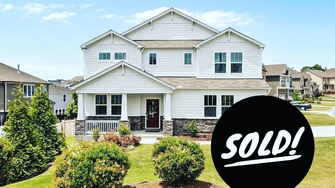 White two-story house with front porch, stone foundation, and a large "Sold!" sign in the yard.