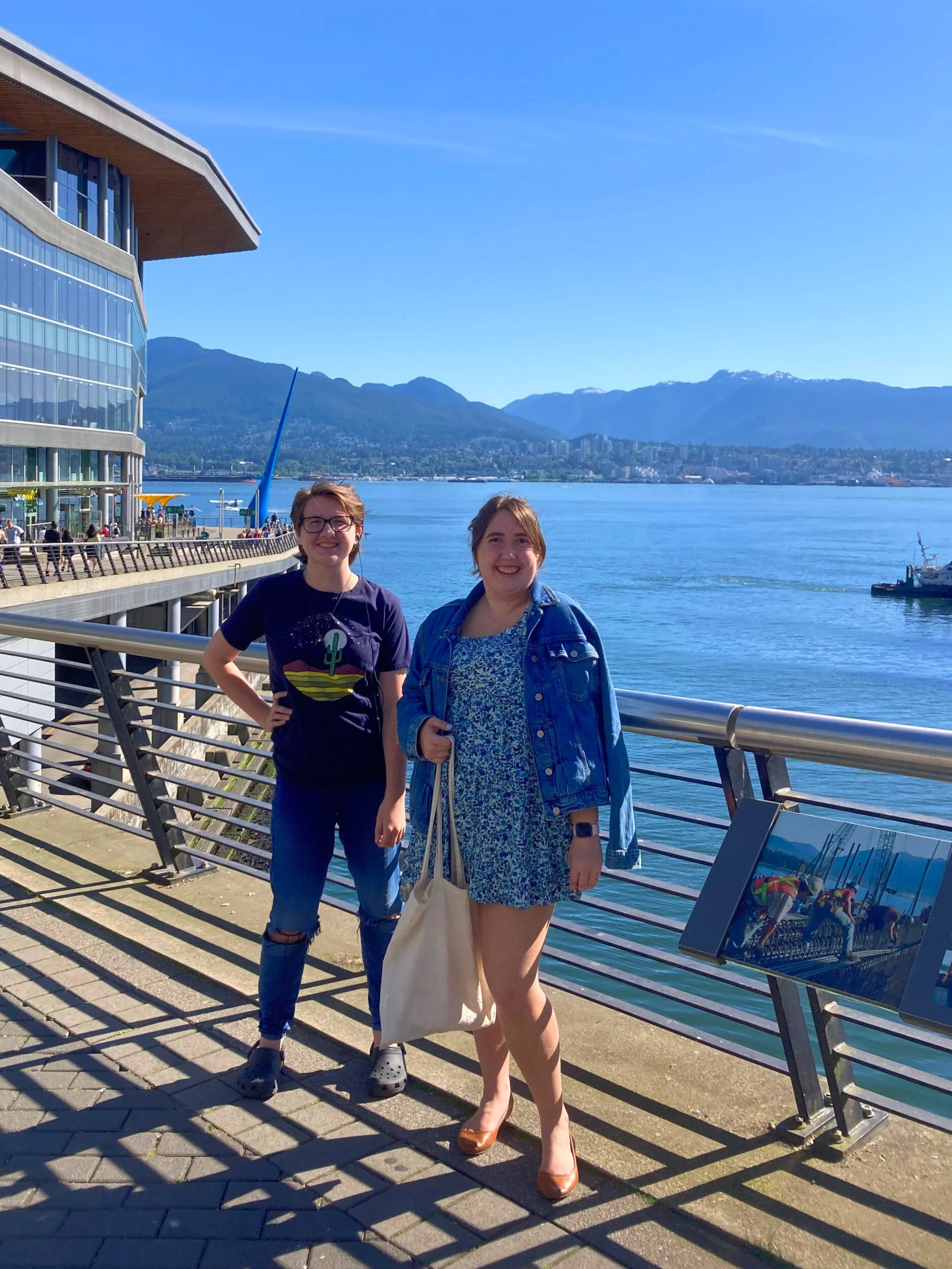 In Vancouver, Maggie's two children are standing on a walking path by the ocean and the mountains.