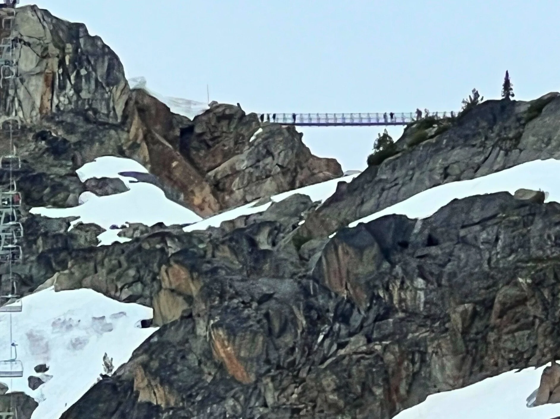 In Whistler, while going up a gondola, snow covered mountains are visible. There is a walking bridge between two mountains.
