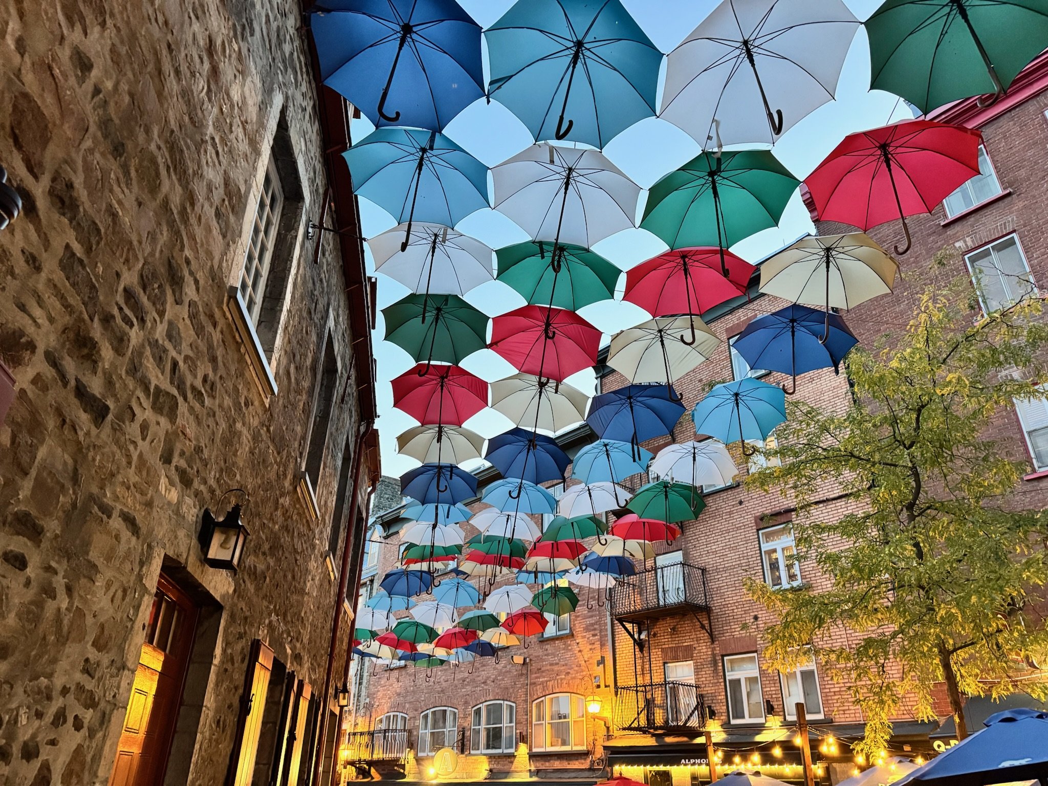In Old Quebec City, in the lower half of the city, colorful umbrellas hang in the sky.