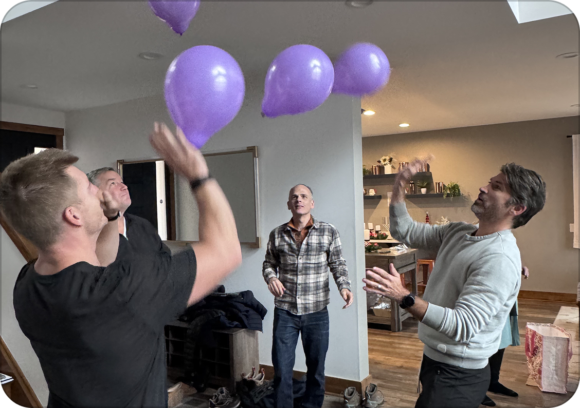 People in a living room playing or celebrating with purple balloons.
