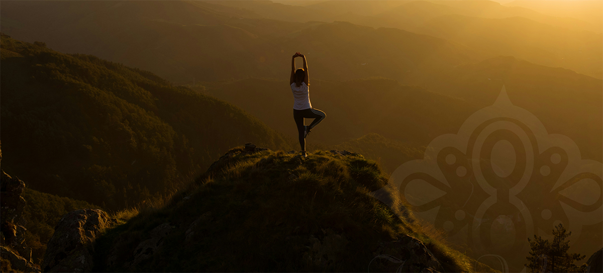 woman doing yoga pose overlooking the sunset on a mountain.