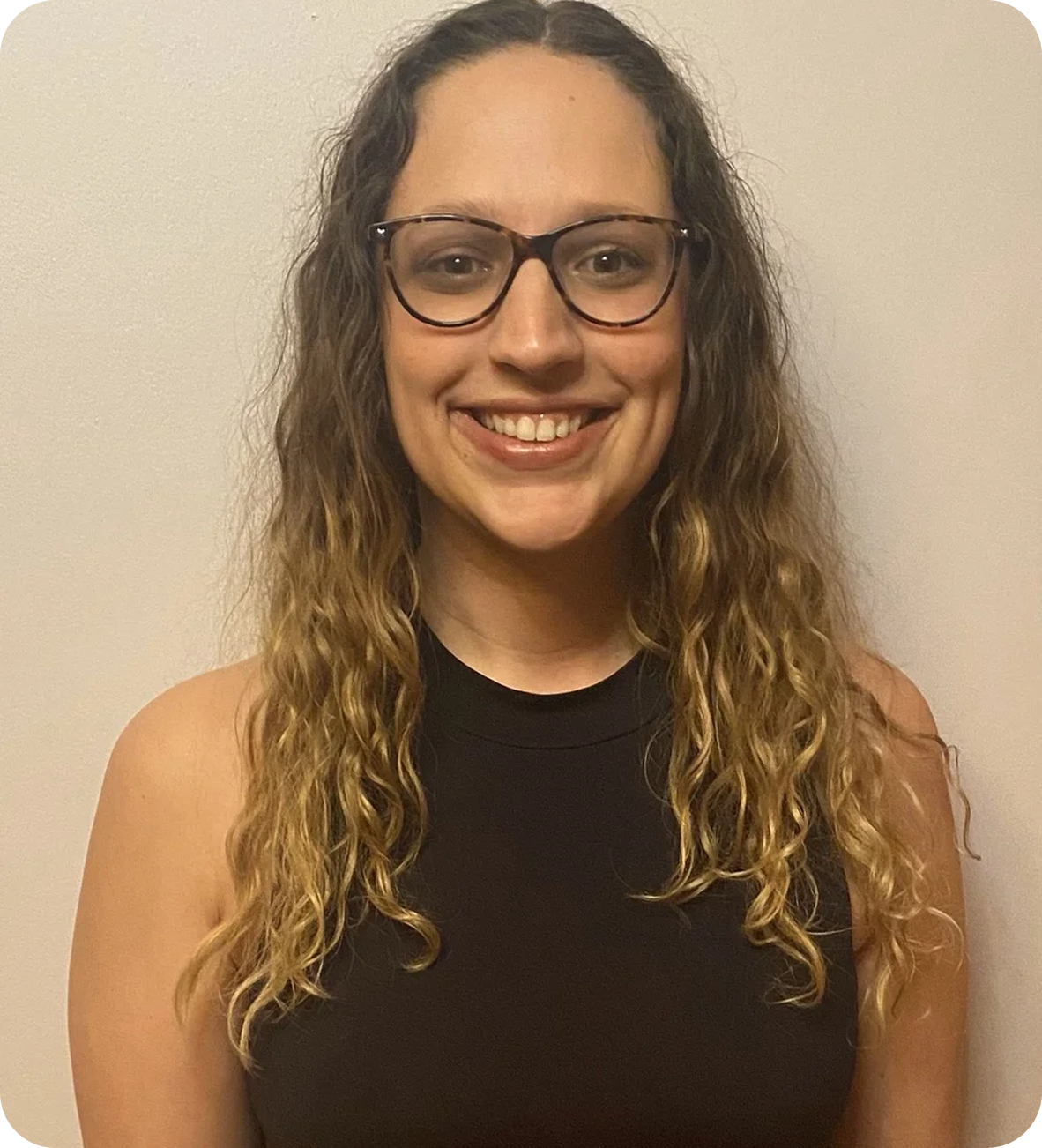 A young woman with curly hair, glasses, and a black sleeveless top smiling at the camera against a neutral background.