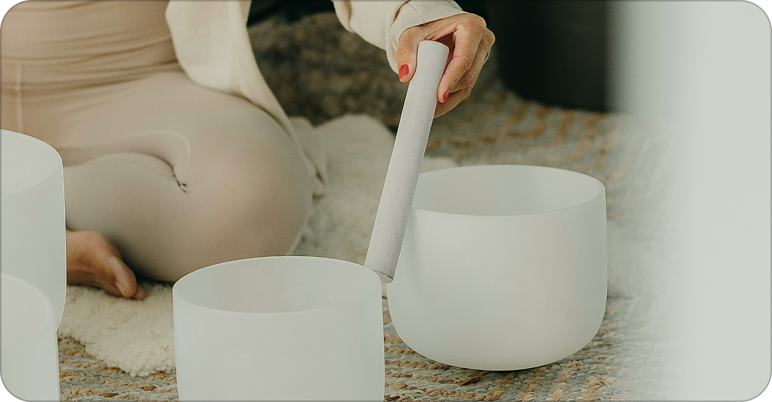 Person playing singing bowls on a textured rug.